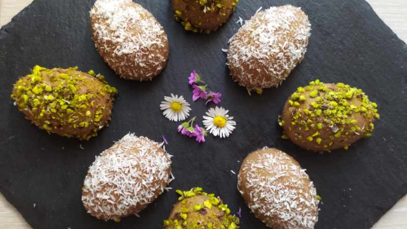 Assorted chocolate truffles decorated with coconut shavings and chopped pistachios, presented on a slate board with small flowers as ricette pasquali garnish.