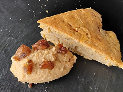 A slice of cornbread with a dollop of honey butter on a dark slate surface.
